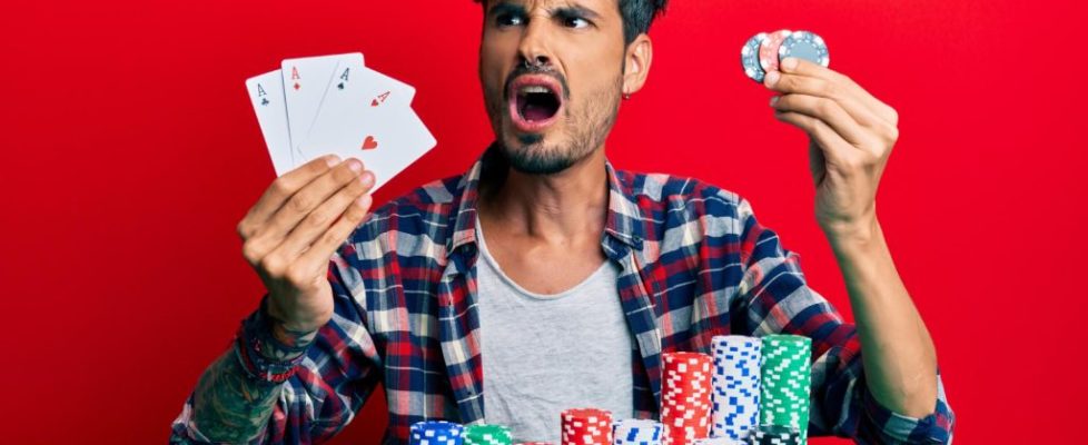 young-hispanic-man-playing-poker-holding-cards-casino-chips-angry-mad-screaming-frustrated-furious-shouting-with-anger-rage-aggressive-concept